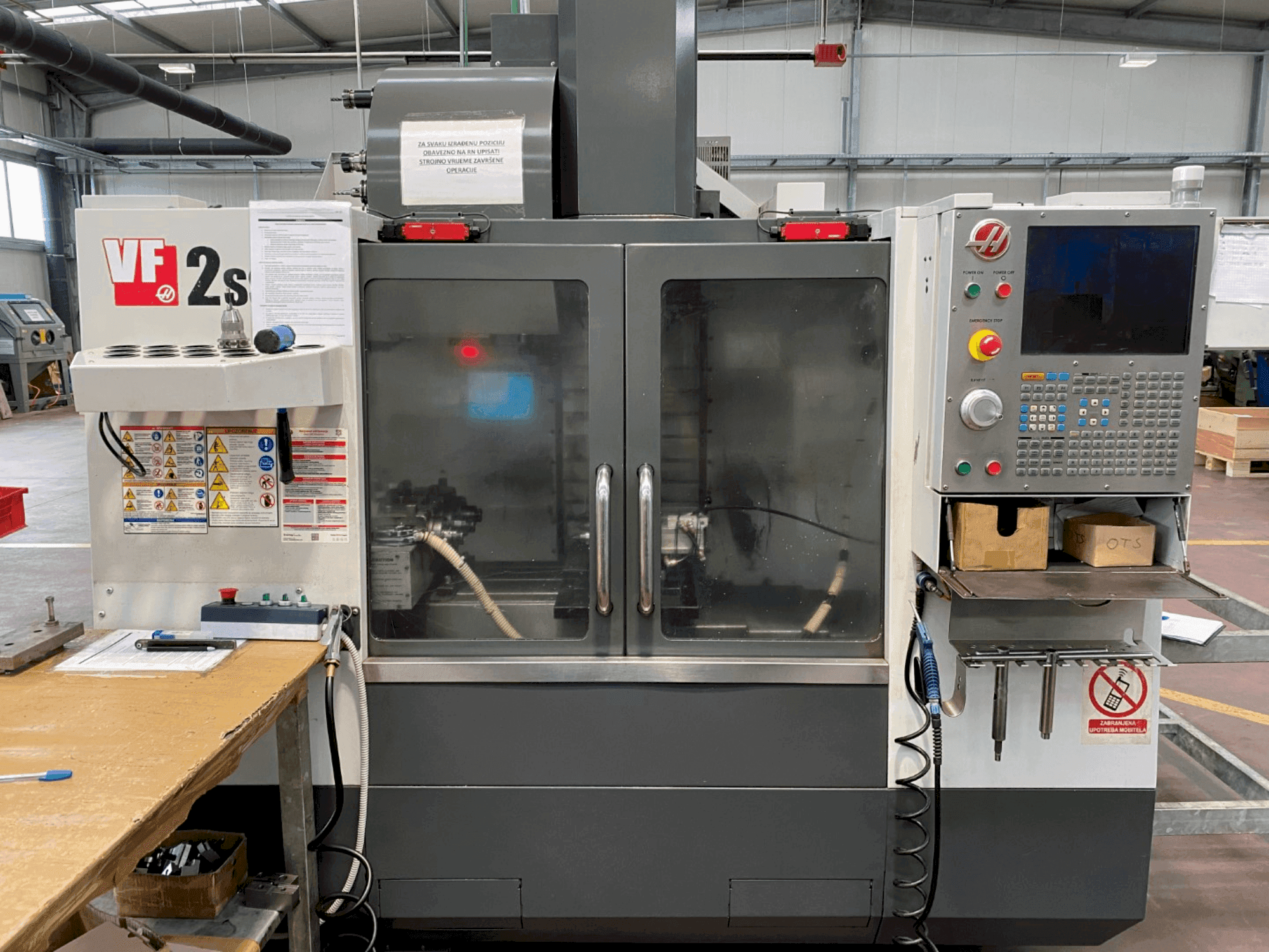 Centro de mecanizado Haas VF-2SS en vista frontal, con panel de control, manguera de refrigerante y etiquetas de seguridad en el lateral.